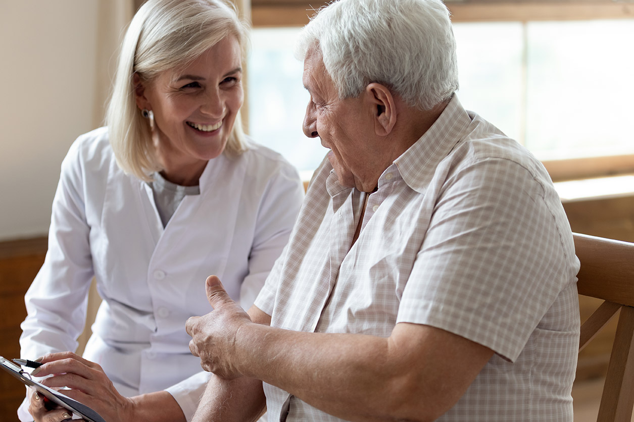 An older man talks to a grey-haired aged care employee.
